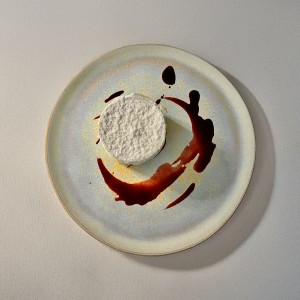 Francesca Rumori Minimalismo Dolce A refined dessert presented as an artistic composition, with a soft, snow-like white layer covering the surface of the treat. The plate is enhanced with strokes of creamy chocolate sauce, creating a perfect visual and flavorful contrast. The minimalist aesthetic and harmonious colors evoke the image of an abstract canvas, inviting imagination and the discovery of delicate and complex flavors. @_designerfra_